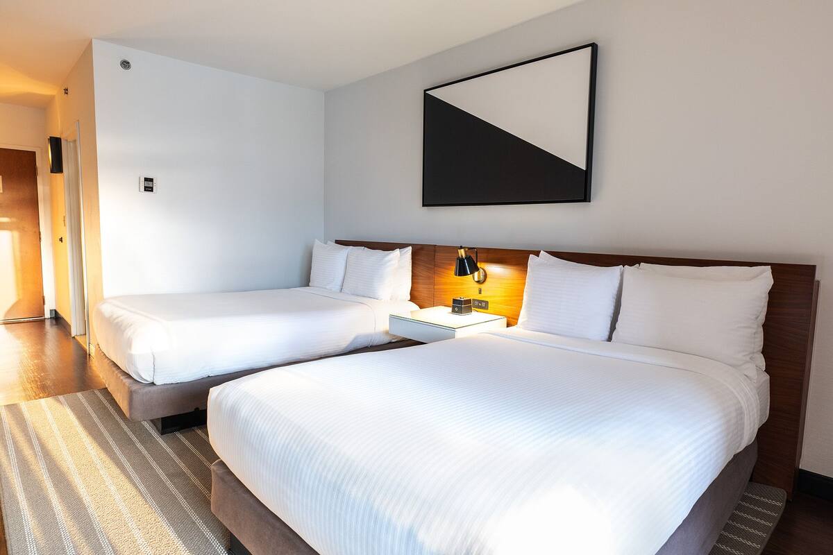 A hotel room with two beds, a nightstand with a lamp, and a framed picture on the wall.