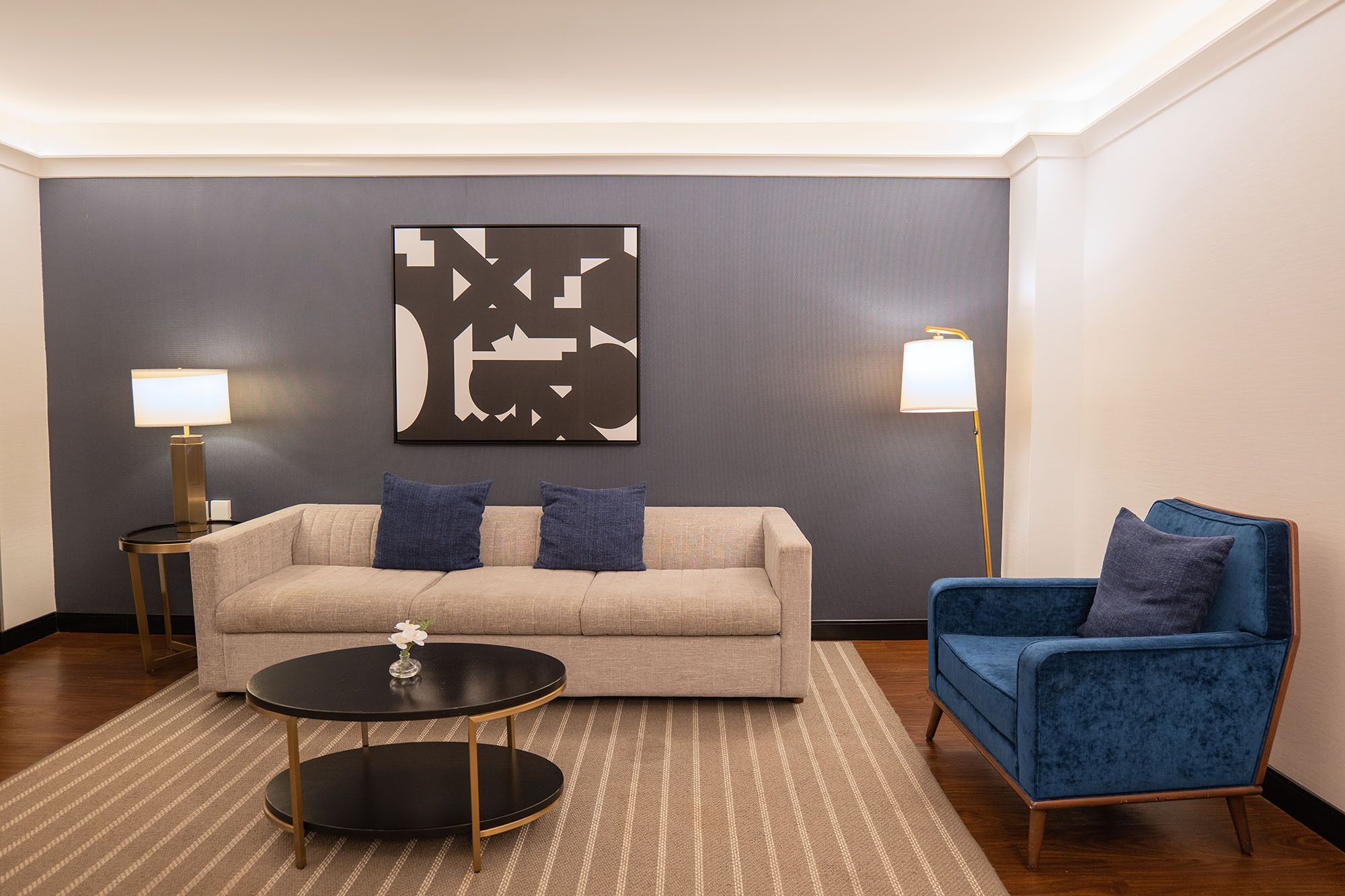 A modern living room with a beige sofa, a blue armchair, a round black coffee table, and two floor lamps.