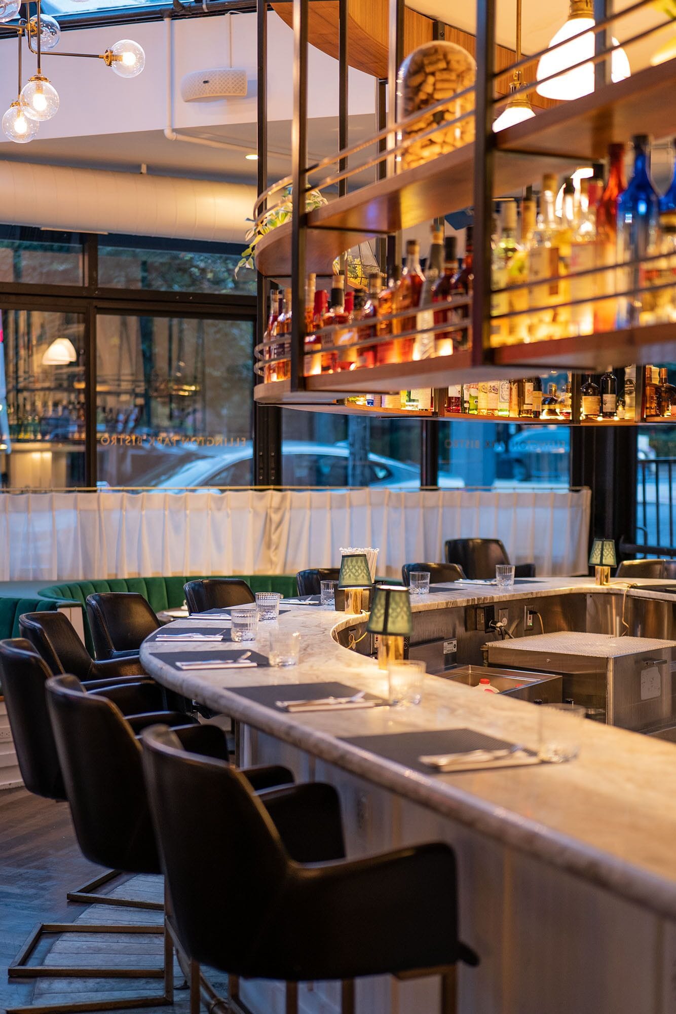 A bar area with a long counter, multiple chairs, and a variety of bottles on shelves.