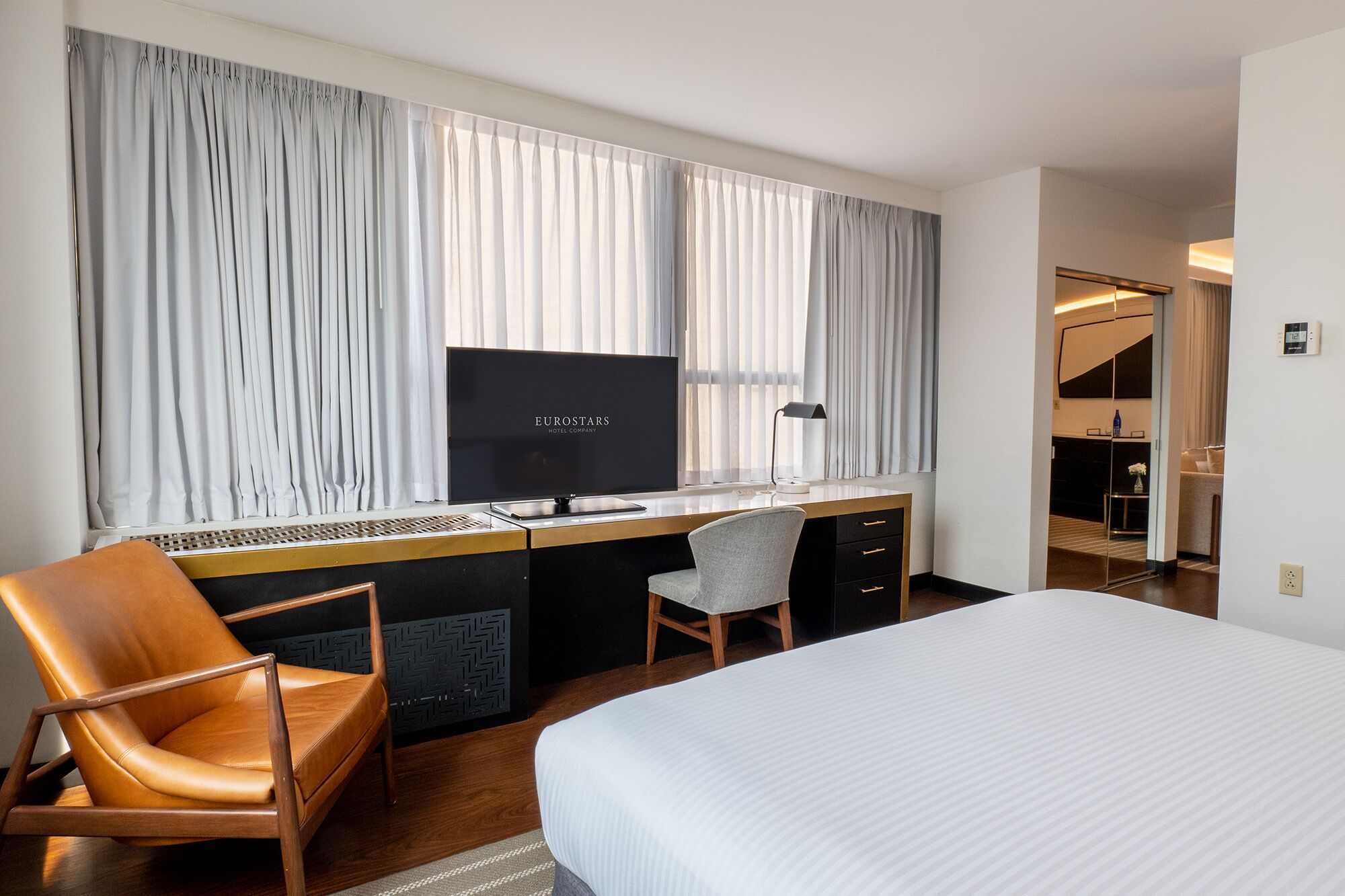 Una habitació d'hotel amb un llit, un escriptori amb un ordinador, una cadira i una televisió.