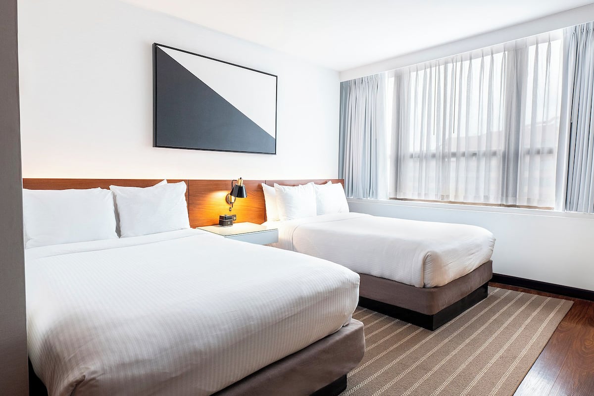 A hotel room with two beds, a nightstand, a lamp, a framed picture, and a window with curtains.
