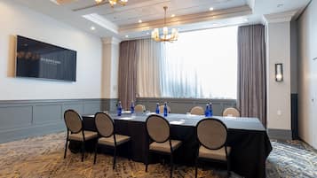 Uma sala de conferência com uma mesa comprida, cadeiras e uma grande janela com cortinas.