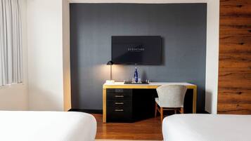 A hotel room with a bed, a desk with a chair, a television mounted on the wall, and a wooden accent wall.