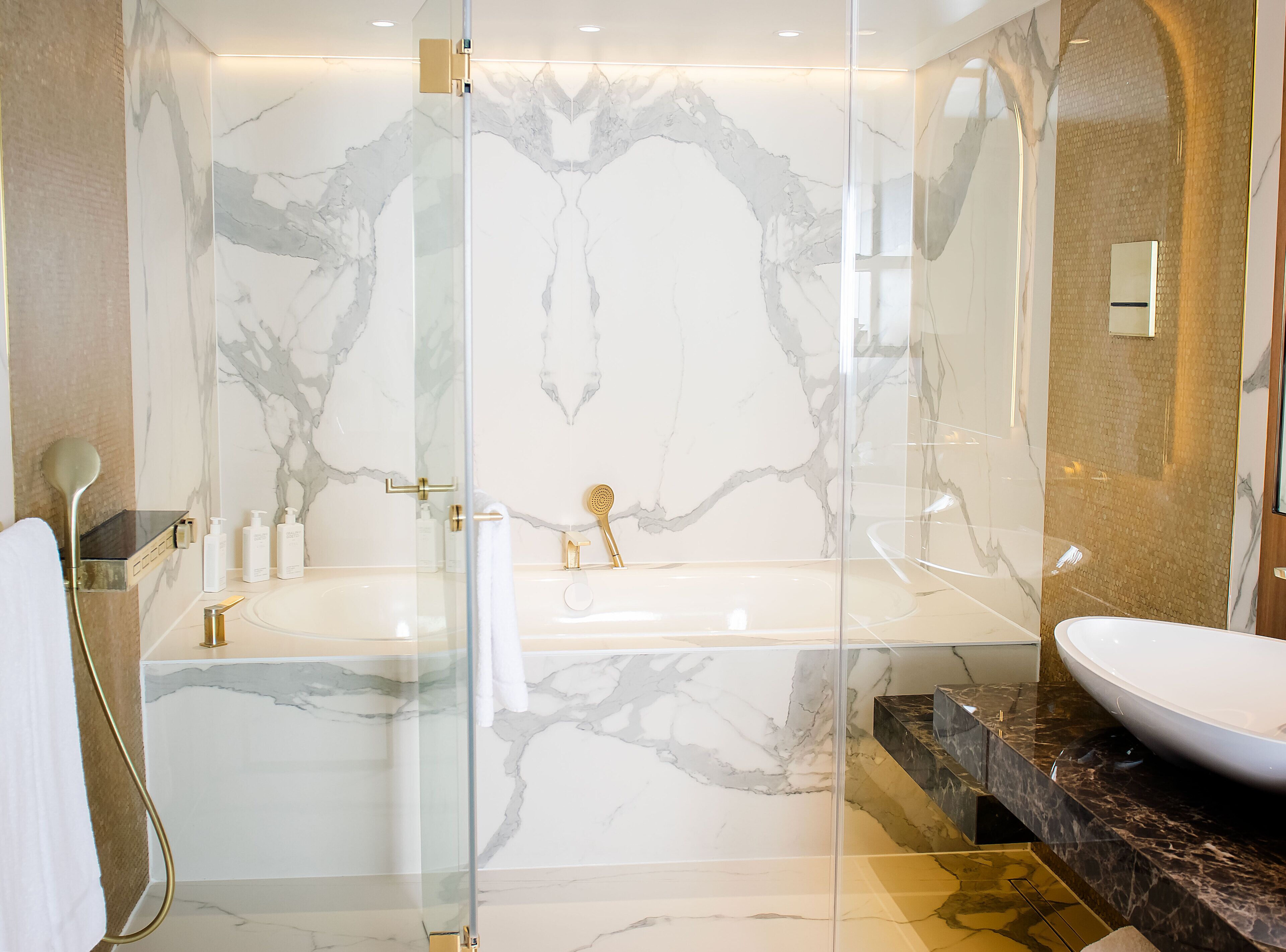 Een moderne badkamer met een marmeren wand, een vrijstaand bad, een douche met glazen wanden en een marmeren blad met een wastafel.