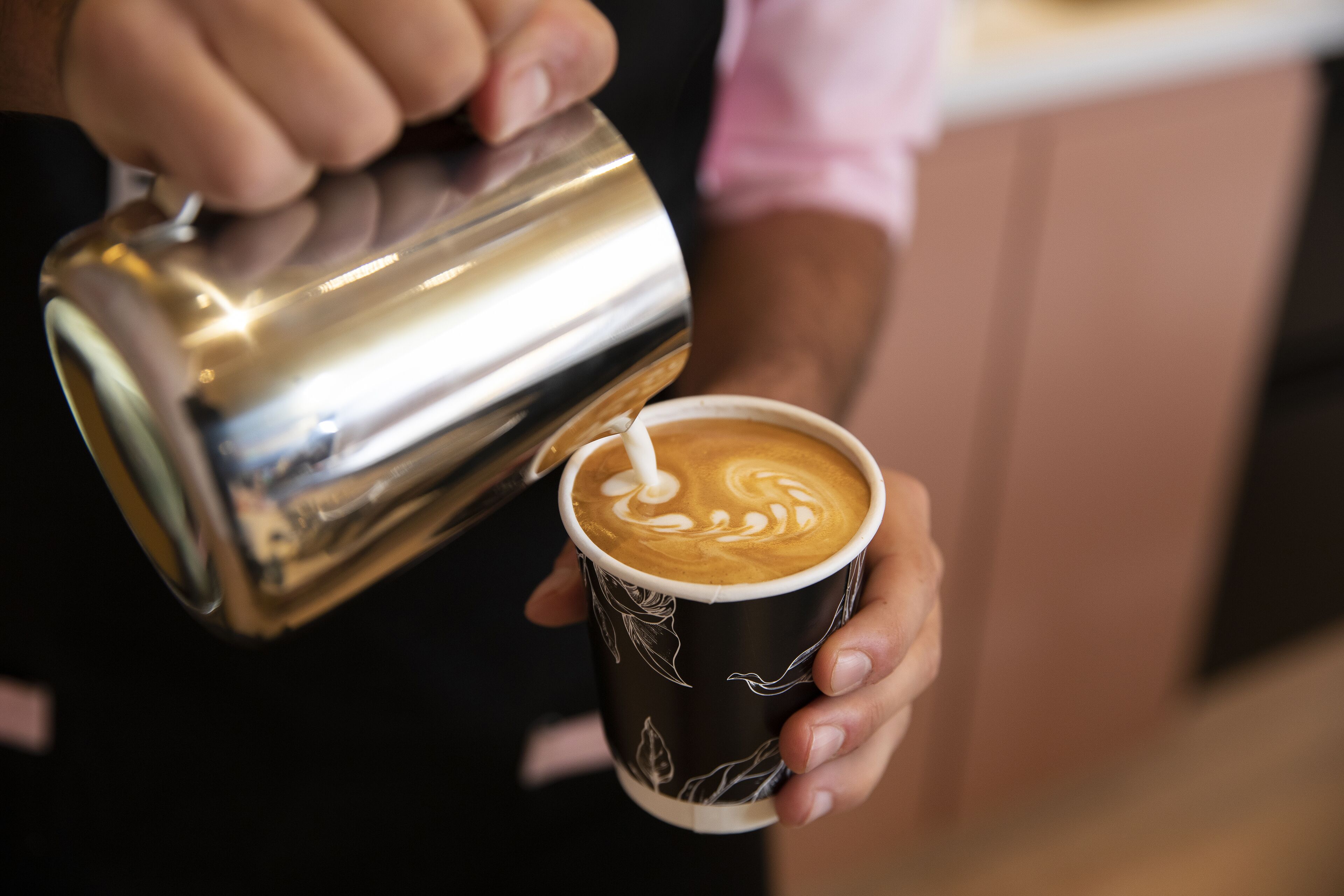 A person pouring steamed milk into a cup of coffee, creating a latte art design.