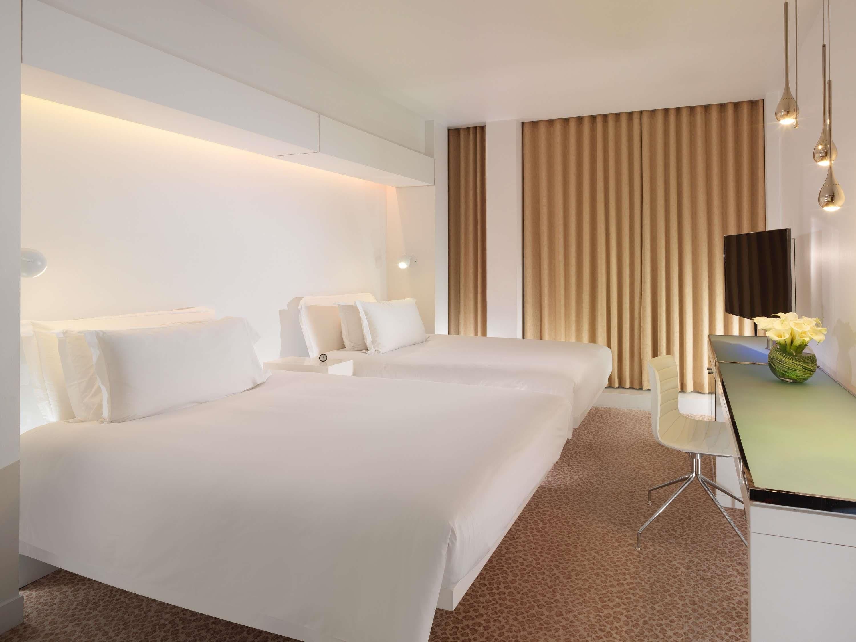 Habitación de hotel con dos camas, un escritorio, una silla, un televisor y un florero con flores.