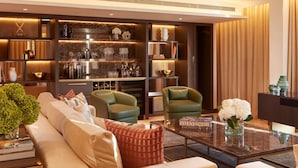 Una sala moderna con un sofá, dos sillones, una mesa de centro y una estantería llena de libros y objetos decorativos.