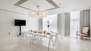 A spacious, modern dining room with a large table set for six, surrounded by clear chairs. A chandelier hangs from the ceiling, and a flat-screen TV is mounted on the wall. - St Martins Lane London, a Morgans Originals hotel (London)