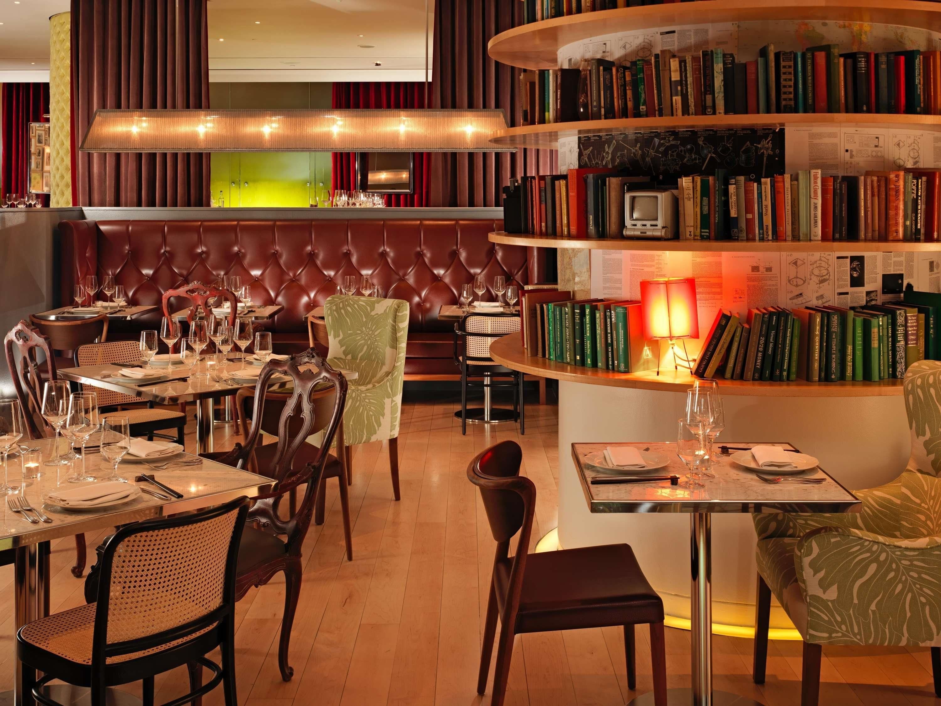 A restaurant interior with leather booth seating, round tables, and a bookshelf filled with books.