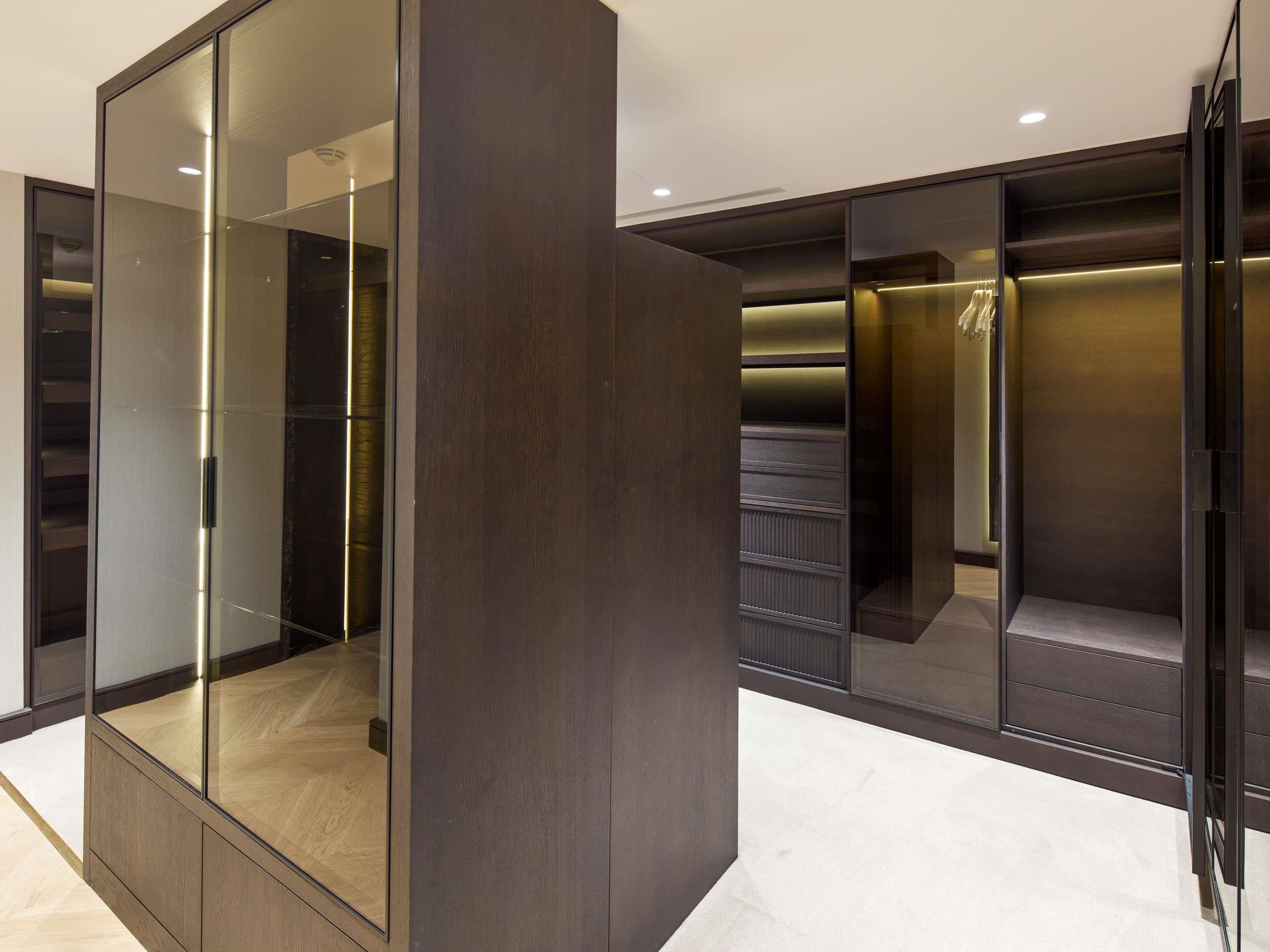 Un dressing moderne et bien éclairé, doté de portes miroir et d’éléments de rangement intégrés.