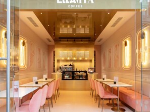 A coffee shop interior with tables and chairs, a counter with a menu, and a display case. - St Martins Lane London, a Morgans Originals hotel (London)
