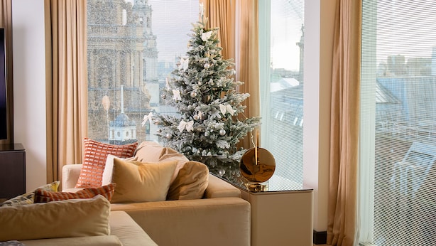A modern living room with a beige sofa, a Christmas tree, and a large window with blinds. - St Martins Lane London, a Morgans Originals hotel (London)