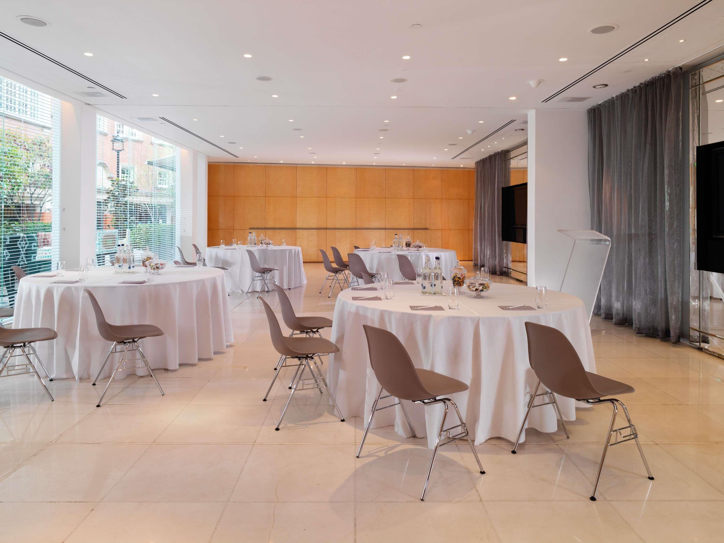 Uma sala de conferência com várias mesas redondas, cadeiras e uma tela grande.