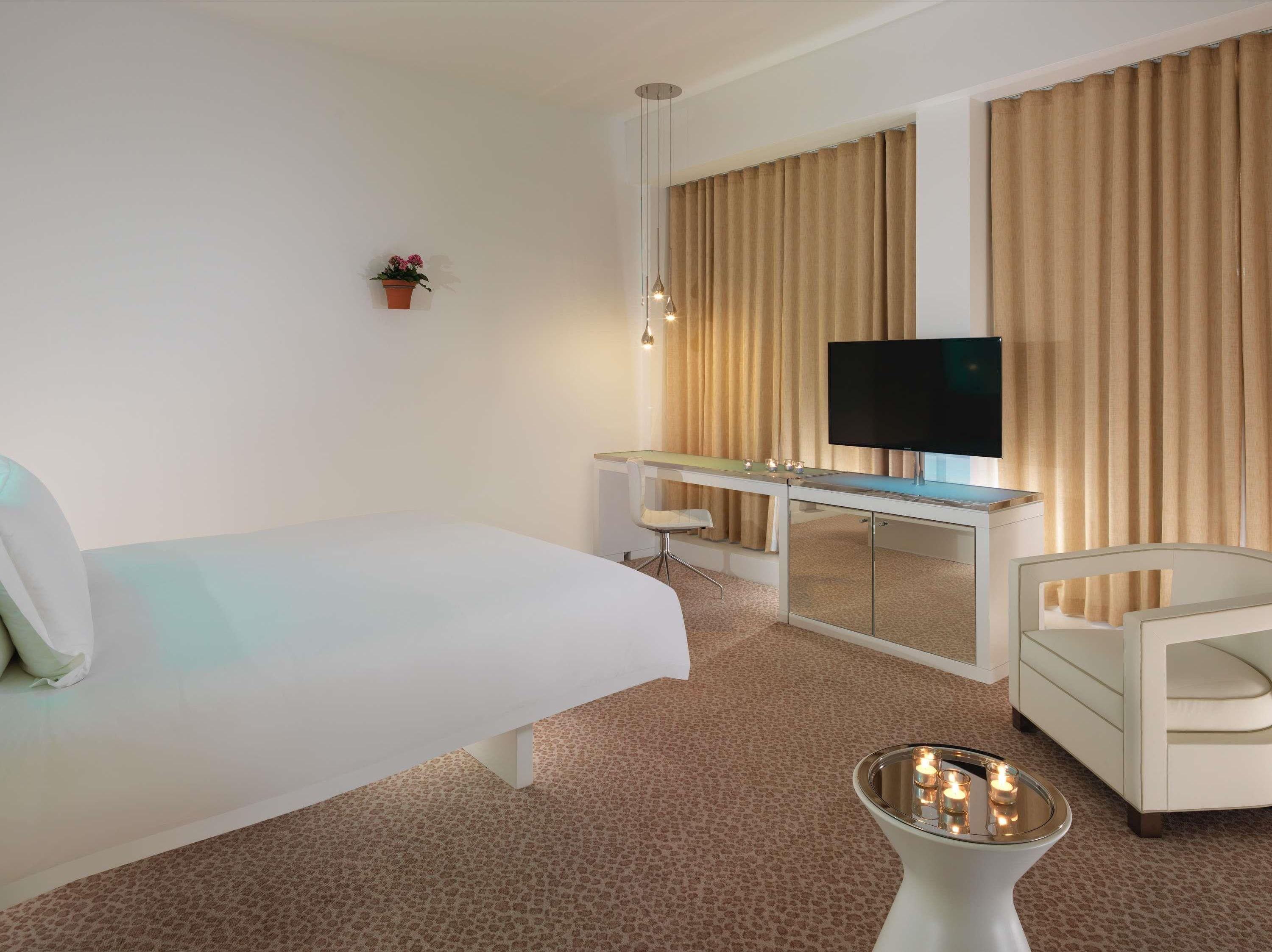 A hotel room with a bed, a desk with a TV, a chair, and a small table with candles.