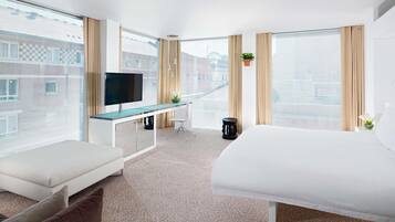 Una habitación de hotel moderna con una cama, un televisor, un escritorio y ventanas amplias.