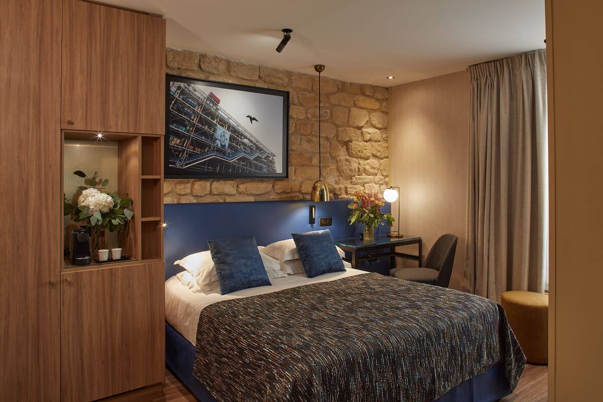 Une chambre d’hôtel avec un grand lit, un bureau, une chaise, une machine à café et un tableau encadré au mur.