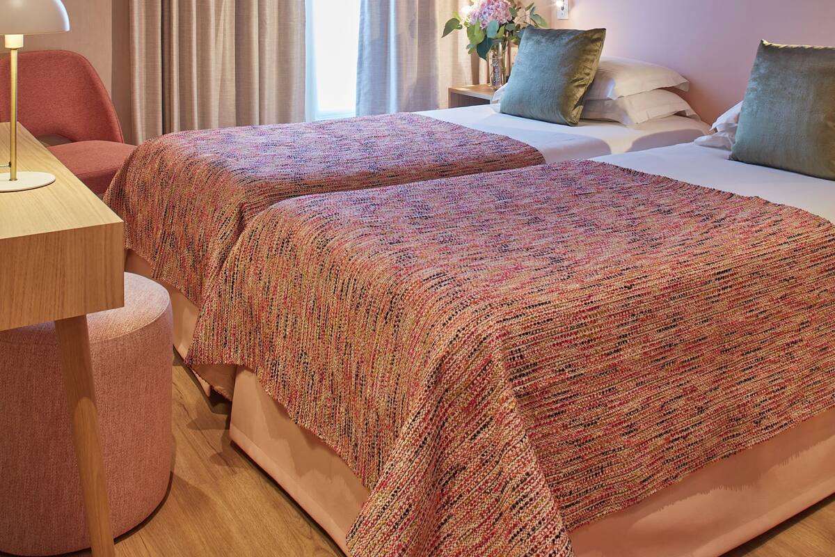 Une chambre d’hôtel avec deux lits, un bureau, une lampe et un tableau au mur.