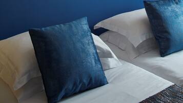 Une chambre d’hôtel avec une tête de lit bleue, du linge de lit blanc et un tableau représentant une scène de rue accroché au mur.