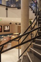 Un moderno vestíbulo de hotel con piso de mármol, una escalera con barandilla negra y una zona de estar con mesas y sillas.