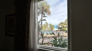 A window with a view of a pool, palm trees, and a building in the background. - Closed - Monumental Movieland Hotel (Orlando)
