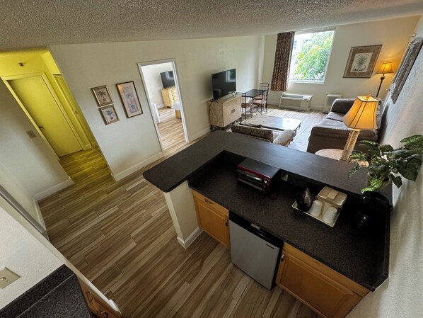 Una cocina compacta con lavavajillas, una zona de comedor con mesa y sillas, un sofá y una ventana con cortinas.