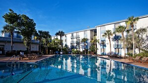 A swimming pool with clear blue water, surrounded by lounge chairs and palm trees, with a building featuring balconies in the background. - Closed - Monumental Movieland Hotel (Orlando)