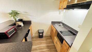 A compact kitchen with a granite countertop, wooden cabinets, a black trash bin, and a small potted plant.