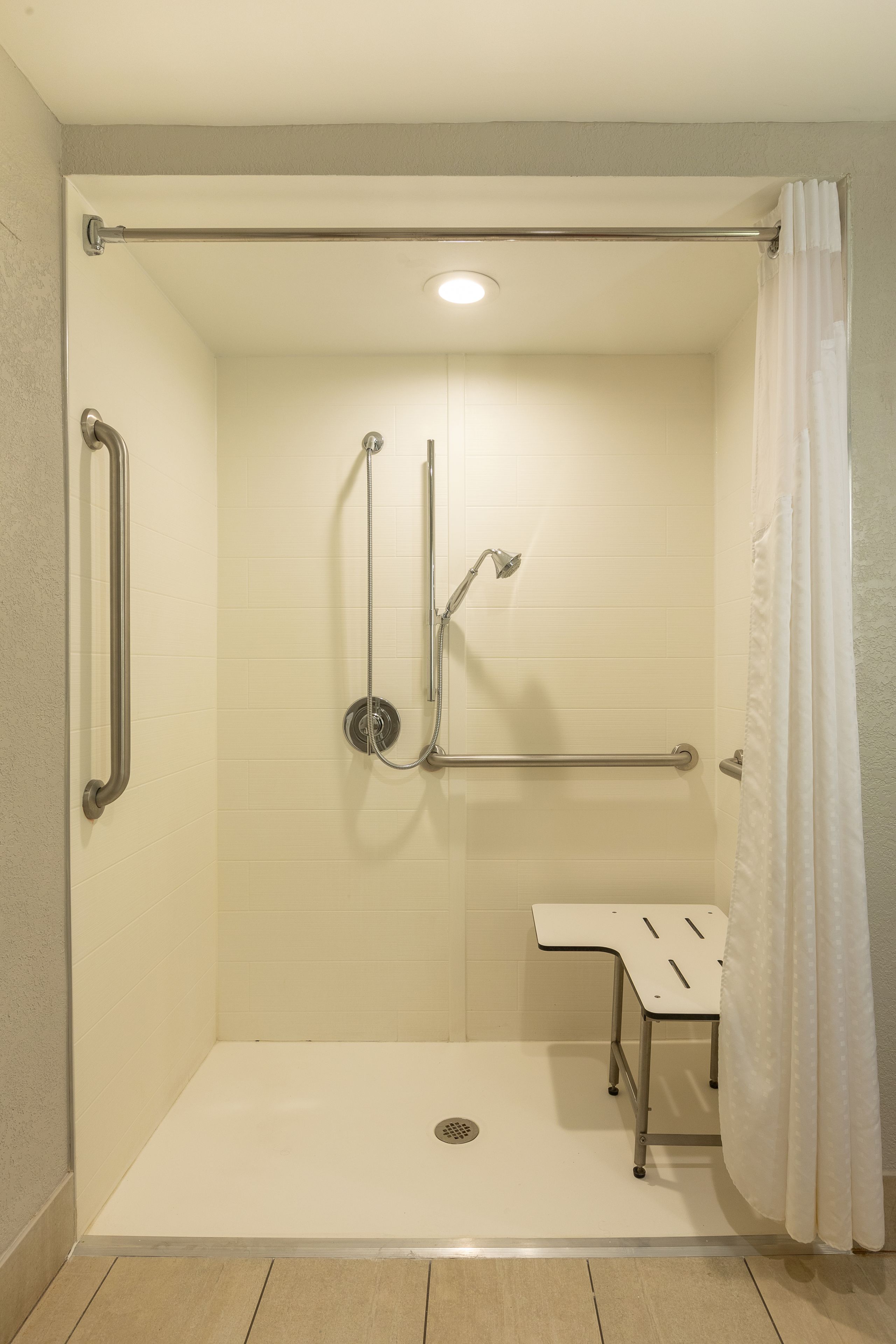 A walk-in shower with grab bars, a handheld showerhead, and a small bench.