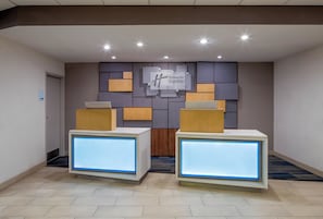 Aula, jossa on kaksi vastaanottotiskiä, seinälle kiinnitetty opastekyltti ja varastotilan opastekyltti.
