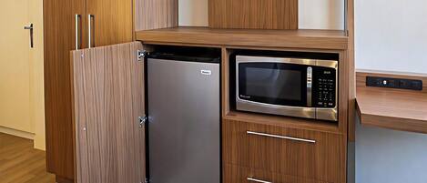 Una kitchenette compacta con microondas integrado, un refrigerador pequeño y un televisor de pantalla plana montado sobre el microondas.