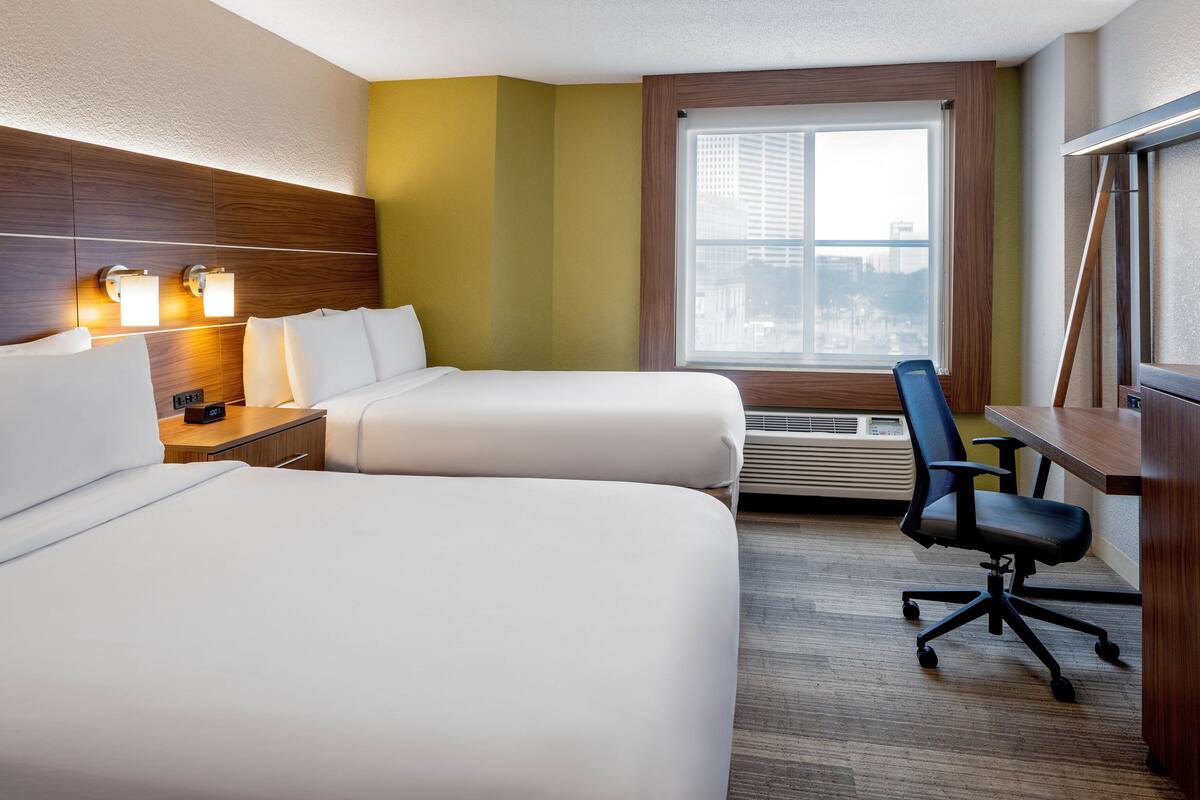 A hotel room with two beds, a desk, a chair, and a large window.