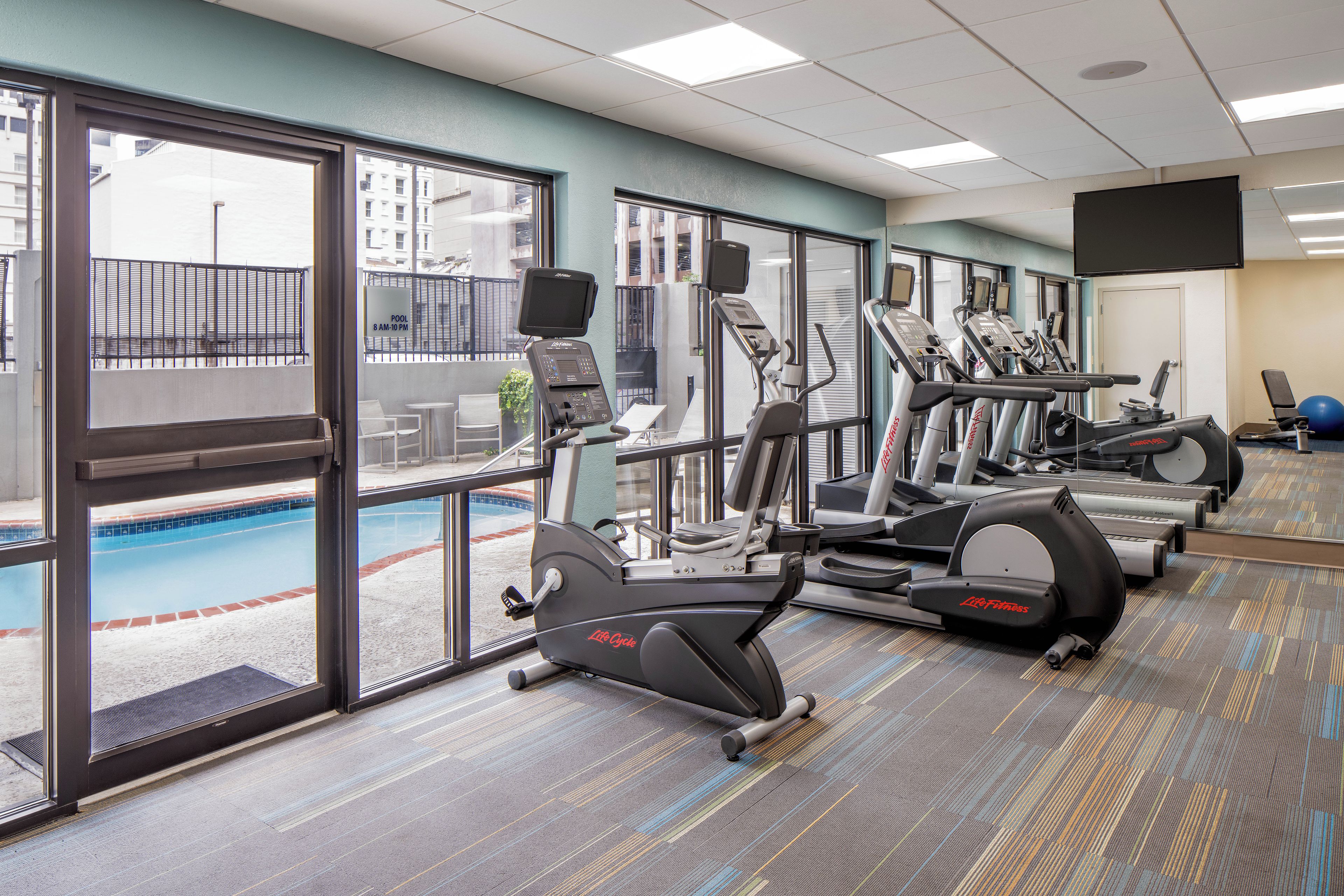 A gym with exercise equipment, a pool, and large windows.