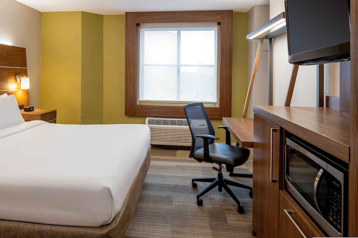 A hotel room with a bed, desk, chair, TV, and a window with blinds.