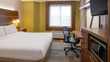 A hotel room with a bed, desk, chair, TV, and a window with blinds.