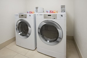 Two front-loading washing machines in a laundry room with tiled flooring and a plain wall. - Holiday Inn Express New Orleans Downtown by IHG (New Orleans)
