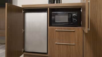 Eine kompakte Küche mit integriertem Kühlschrank und Mikrowelle, ausgestattet mit Holzschränken und einer Edelstahloptik.