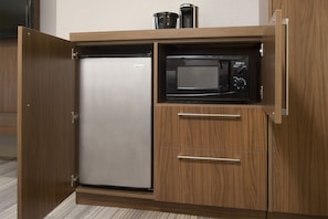 A compact kitchen with a built-in refrigerator and microwave, featuring wooden cabinetry and a stainless steel finish. - Holiday Inn Express New Orleans Downtown by IHG (New Orleans)