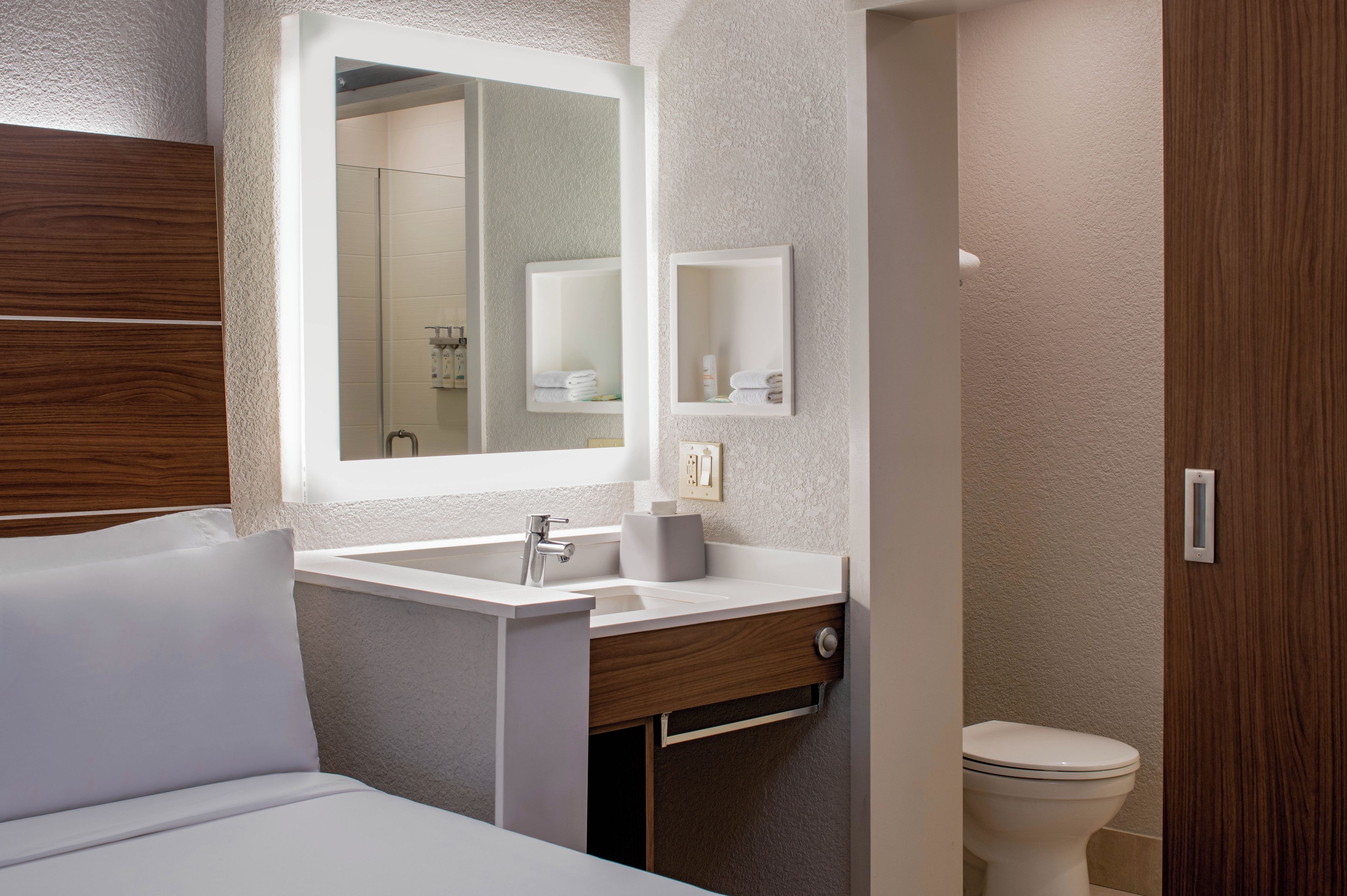 A modern bathroom with a large mirror, a white sink, a wooden vanity, and a toilet.