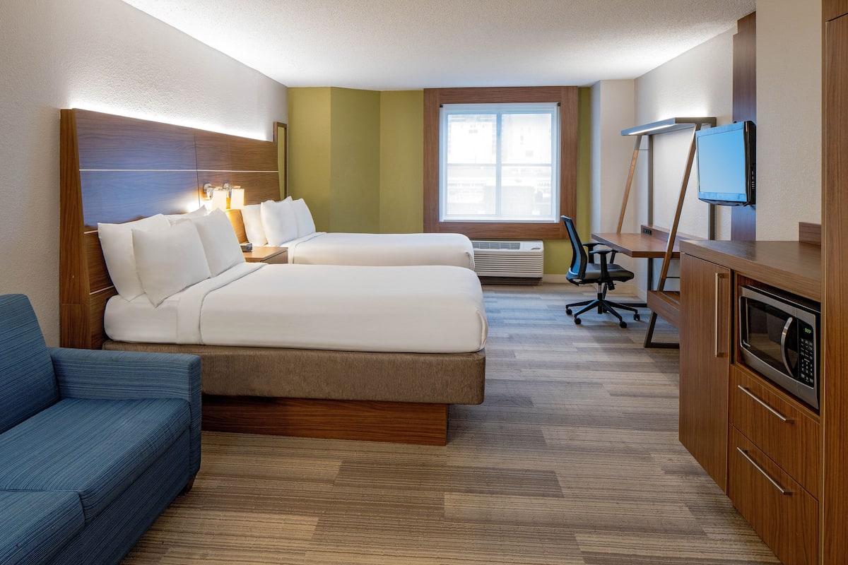 A hotel room with two beds, a desk, a television, a microwave, and a chair.
