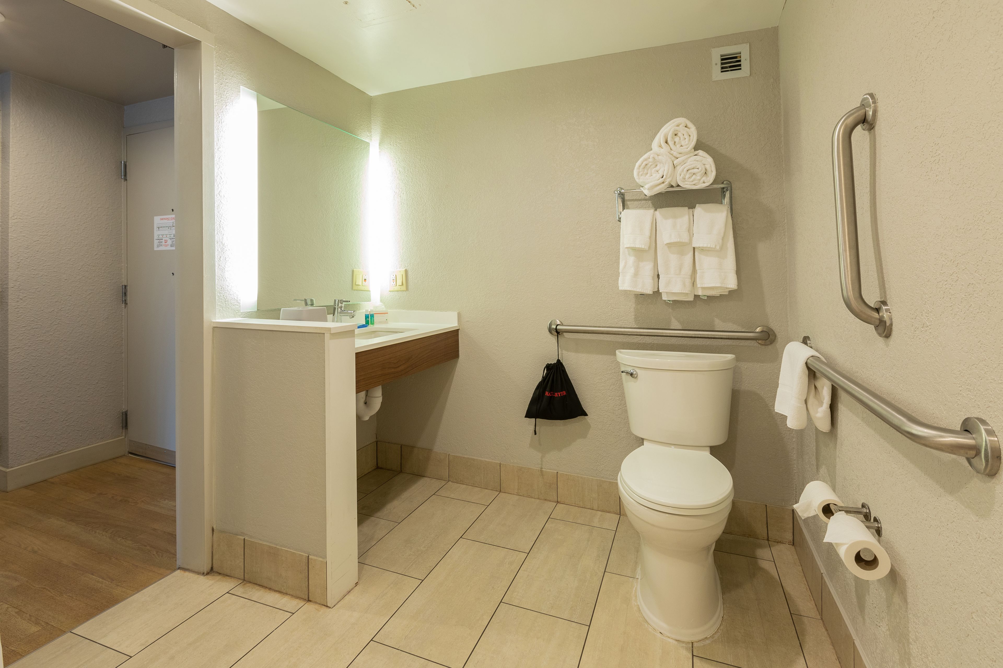 A modern bathroom with a toilet, sink, and handrails.