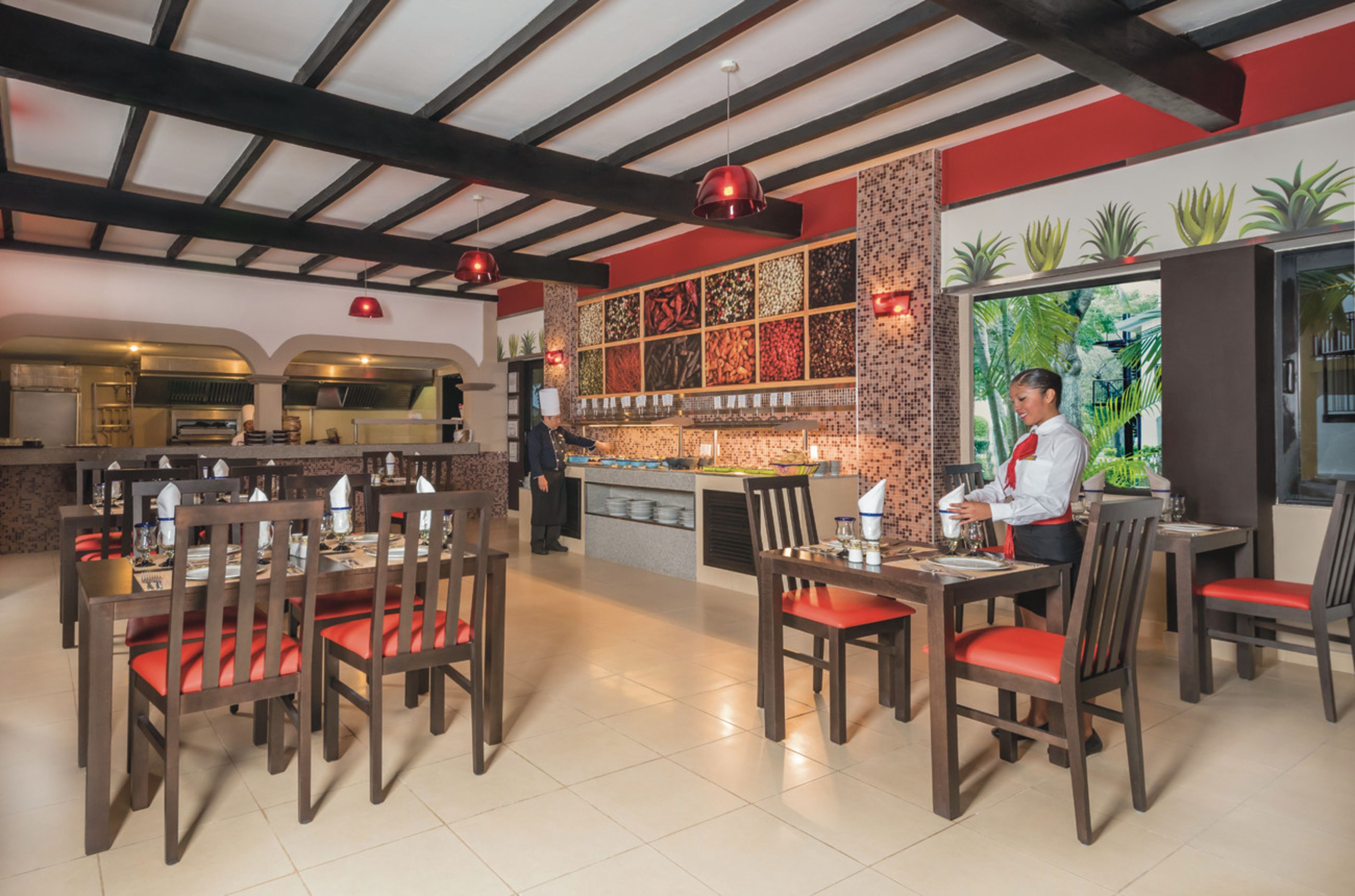 A restaurant with wooden tables and chairs, a kitchen area, and a view of greenery through the window.