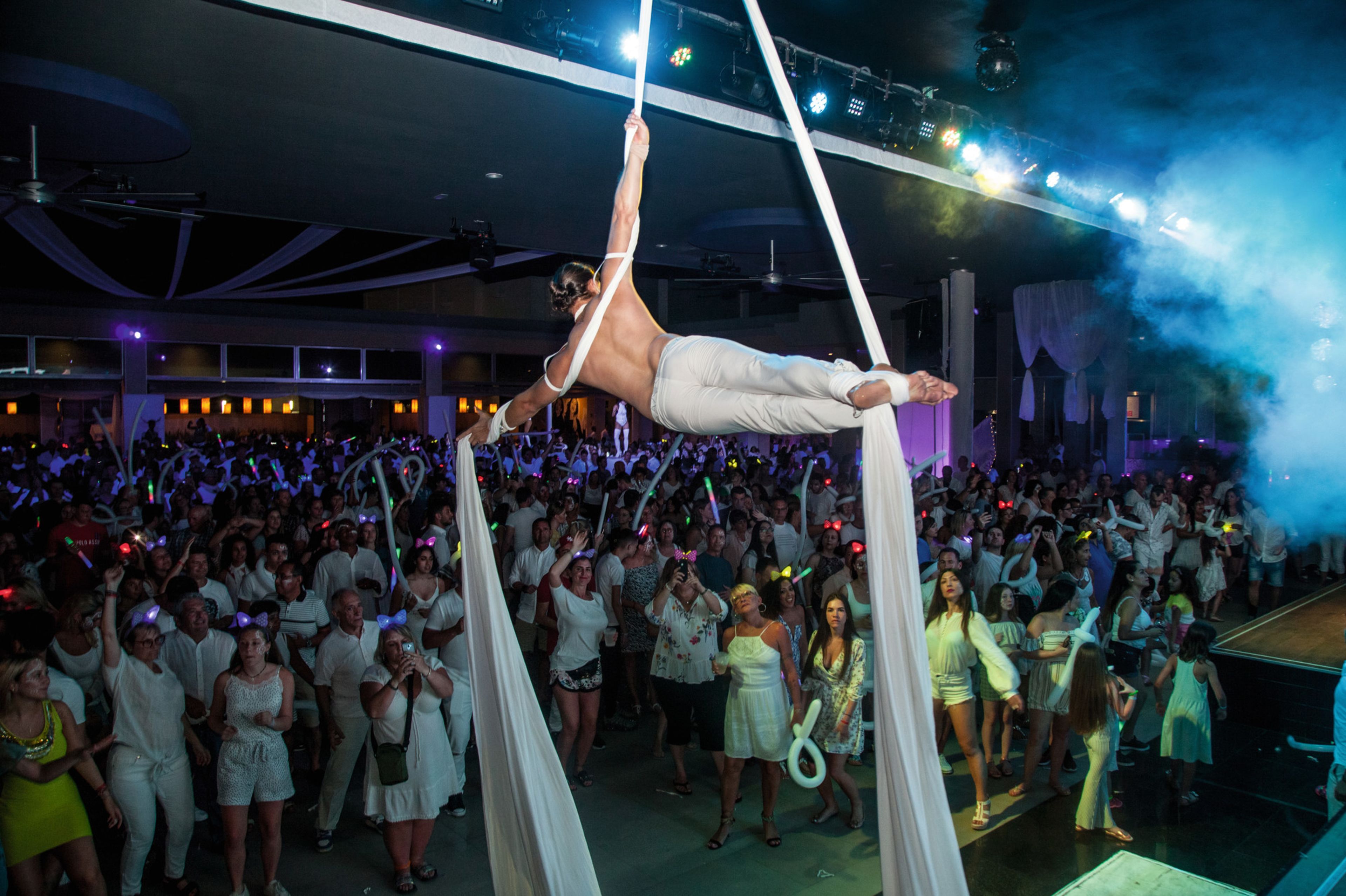 A large indoor venue with a crowd gathered around an aerial performer.