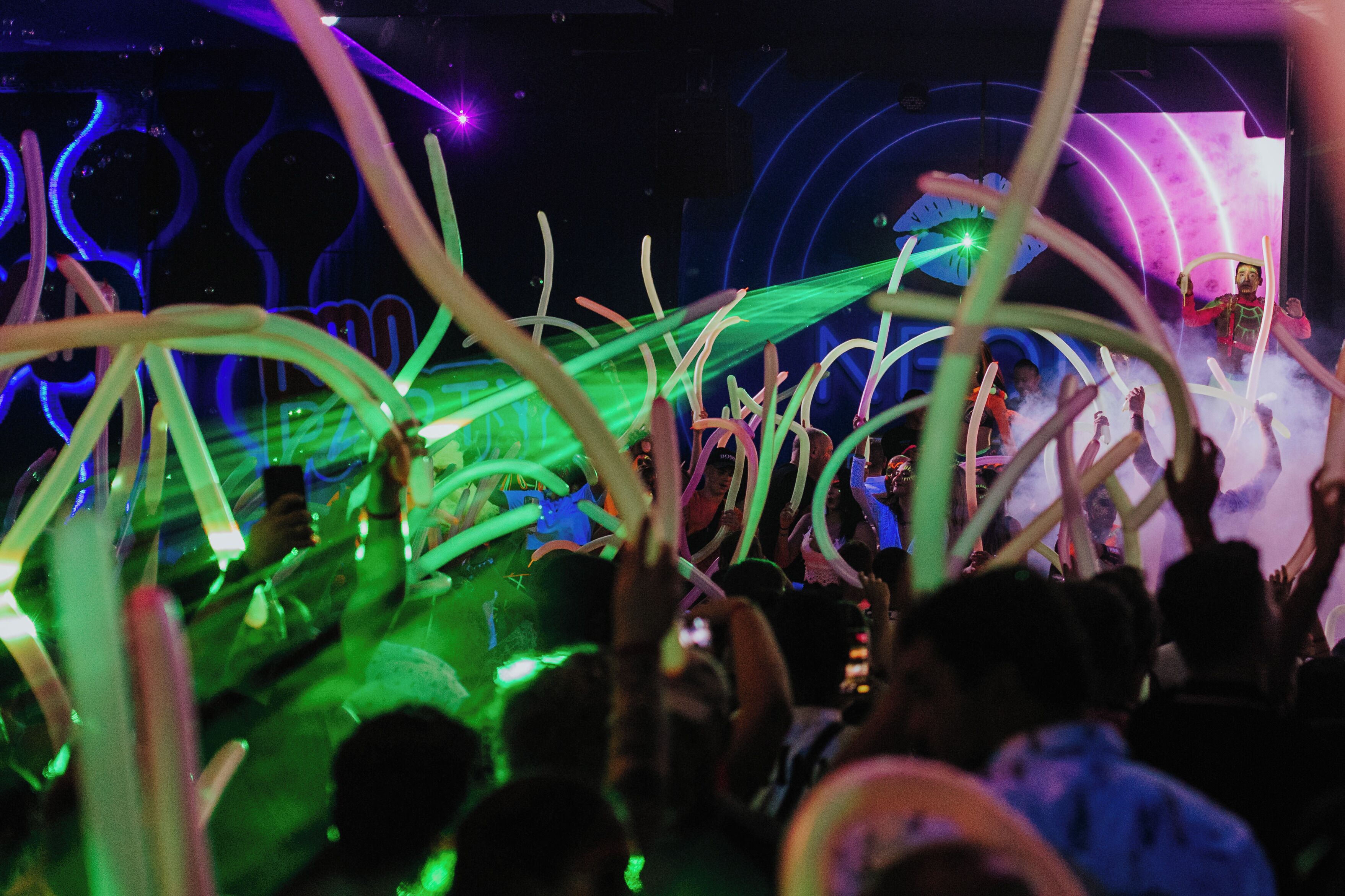 A crowded indoor event with people holding up light sticks, and a stage with a performer in the background.