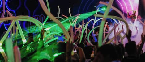 A crowded indoor event with people holding up light sticks, and a stage with a performer in the background.