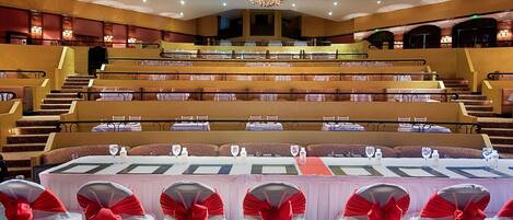Un gran auditorio con asientos en niveles, una araña y mesas con tarjetas de nombres.