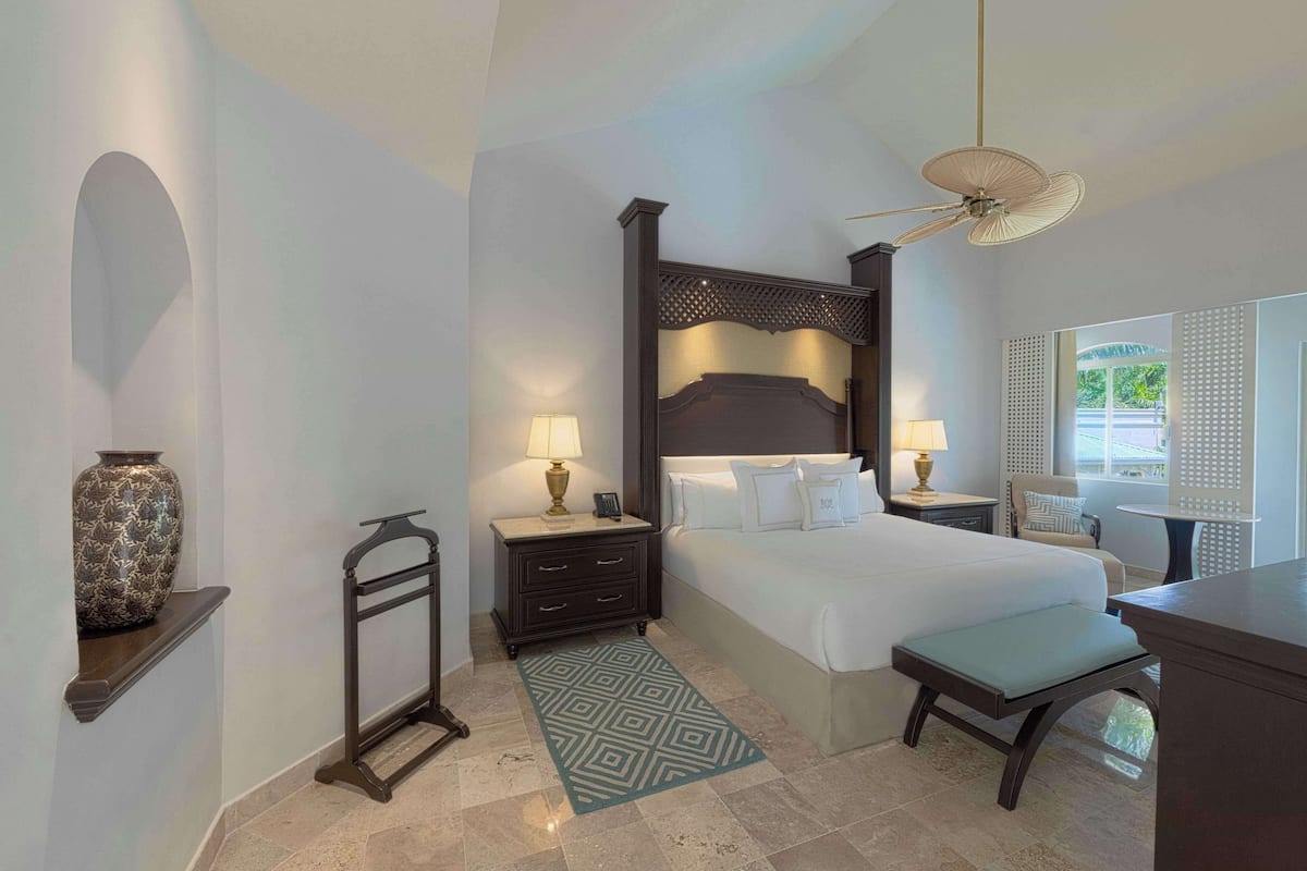 Une chambre d’hôtel avec un grand lit, deux tables de chevet avec des lampes, un bureau, une chaise, un vase décoratif et un tapis à motifs.