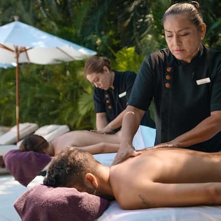A massage therapy session in a tropical setting with lounge chairs and umbrellas.