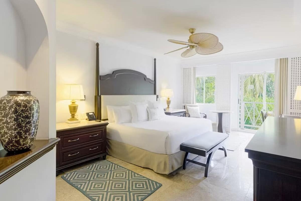 Une chambre d’hôtel équipée d’un lit, de tables de chevet, d’un bureau, d’une chaise, d’une télévision, d’un ventilateur de plafond et d’une fenêtre donnant sur un paysage agréable.
