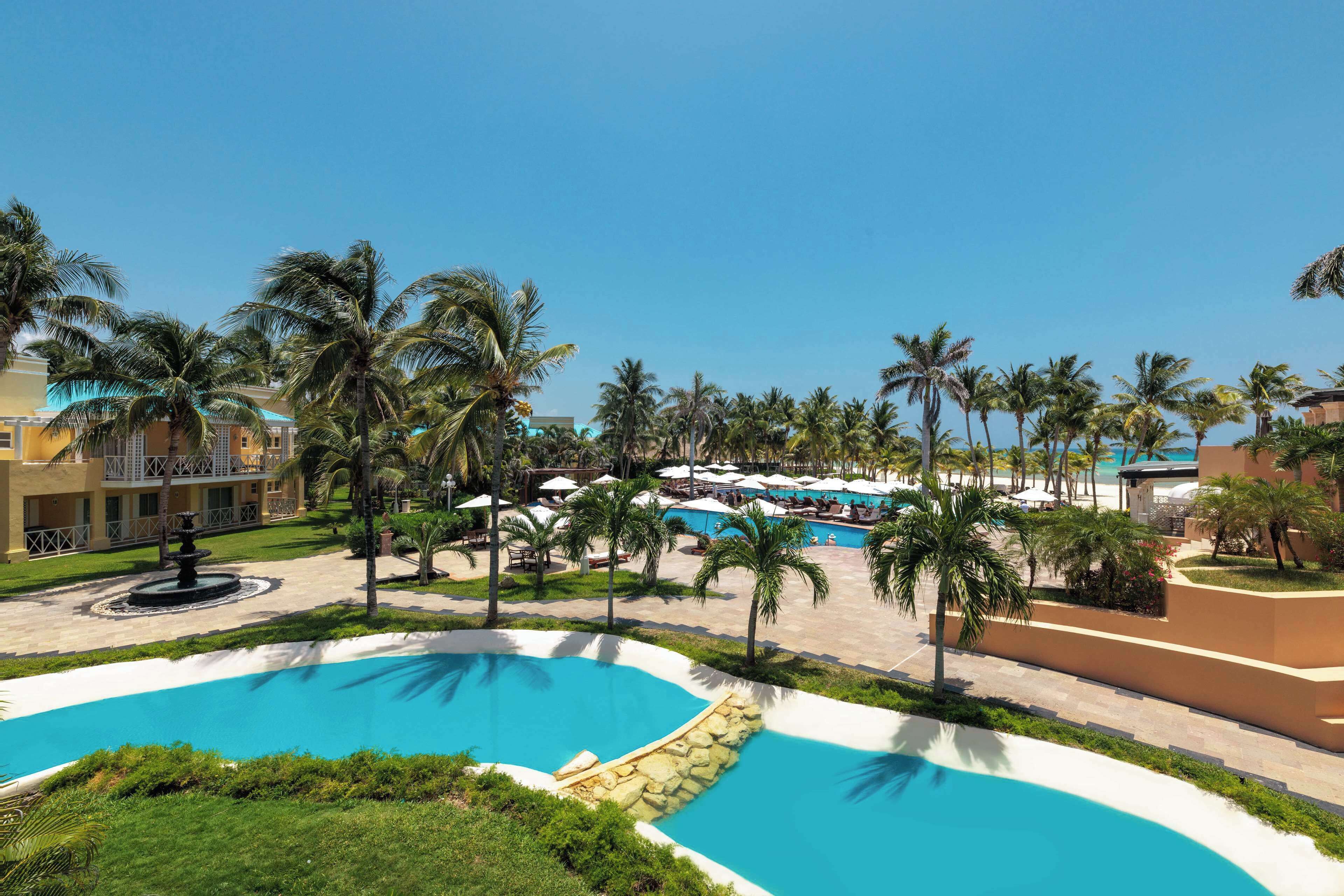 Un resort con varias piscinas, palmeras y un césped bien cuidado.