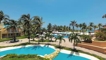 Ein Resort mit mehreren Schwimmbecken, Palmen und einem gepflegten Rasen.